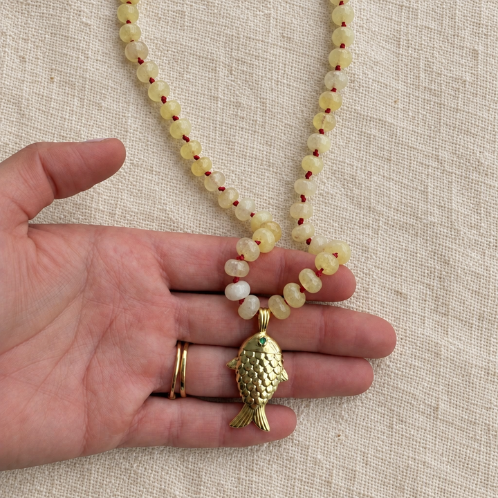 Collar pez en la mano sobre tela rústica crema